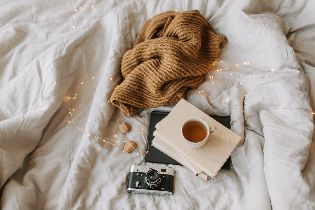 Warm and inviting flat lay featuring a blanket, vintage camera, books, and a cup of tea.